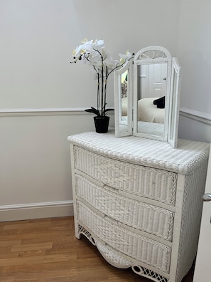 A white wicker dresser with a mirror and a potted orchid.