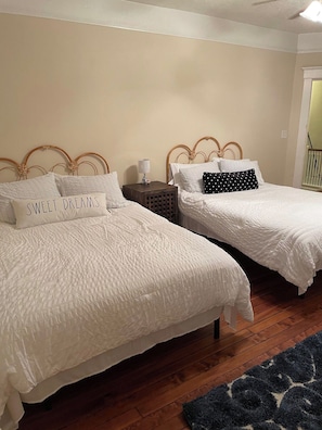 Ein Schlafzimmer mit zwei Betten, jeweils mit weißer Bettwäsche und Kissen, einem kleinen Nachttisch mit Lampe und einem dunkelblauen Teppich auf dem Holzboden.