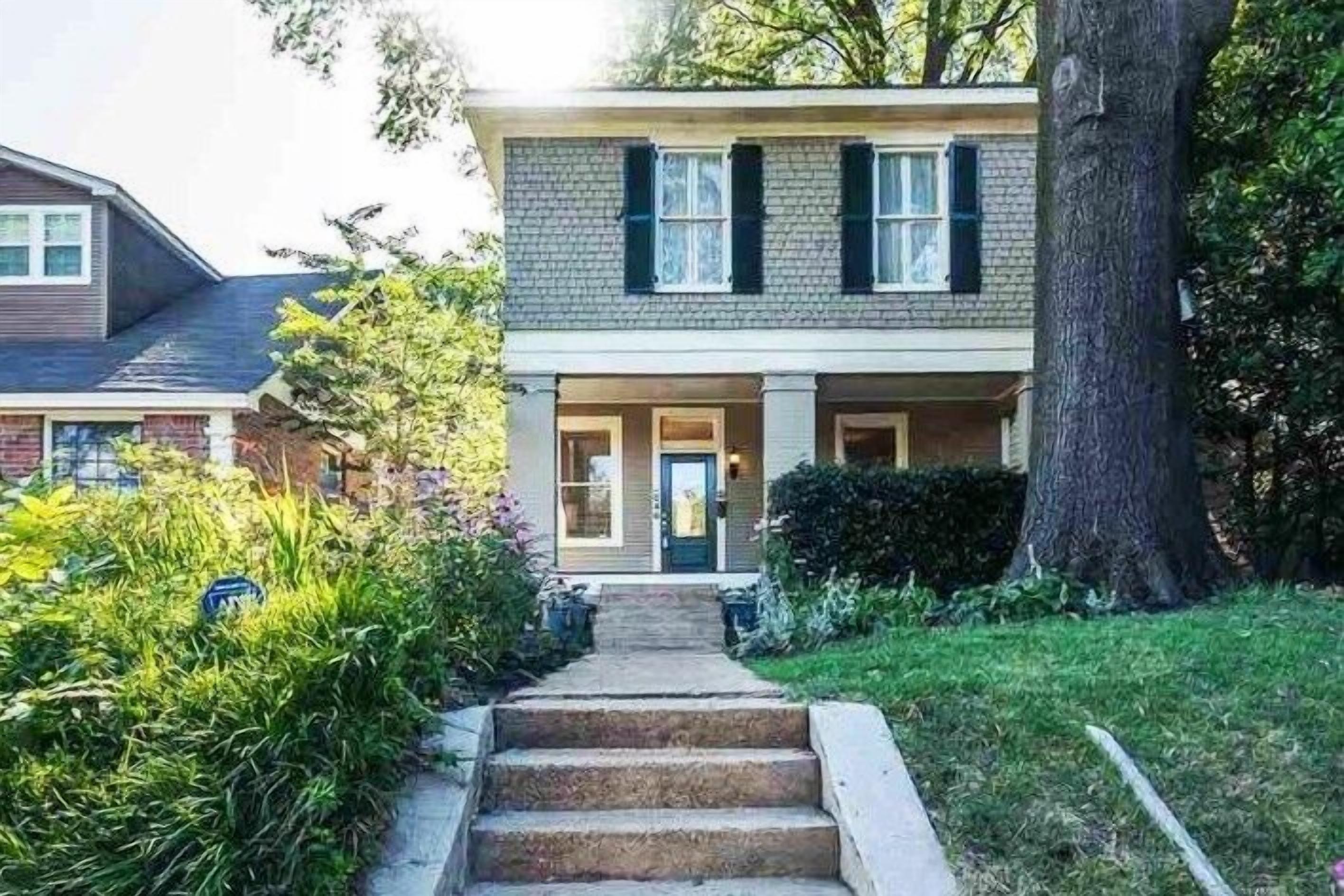 A two-story house with a front porch, a tree in the yard, and a pathway leading to the entrance.
