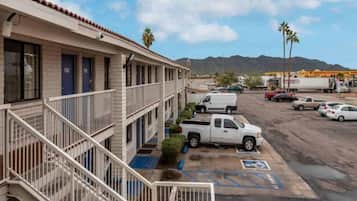 A multi-story motel with a parking lot, a white pickup truck parked in front, and mountains in the background.