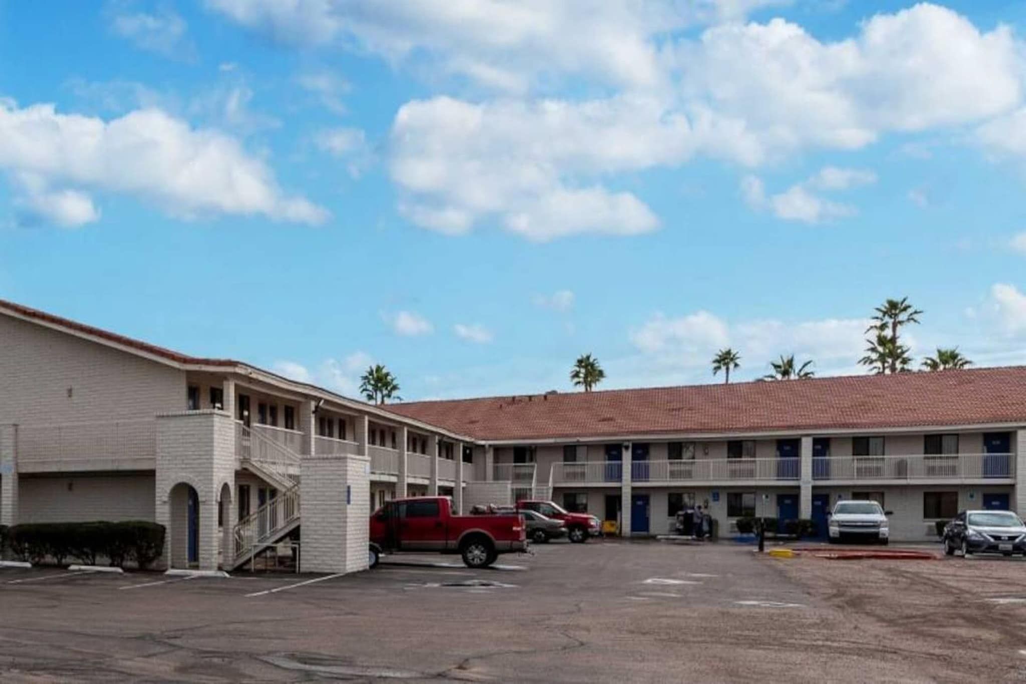 A motel with a parking lot, a red pickup truck, and a two-story building with a red-tiled roof.