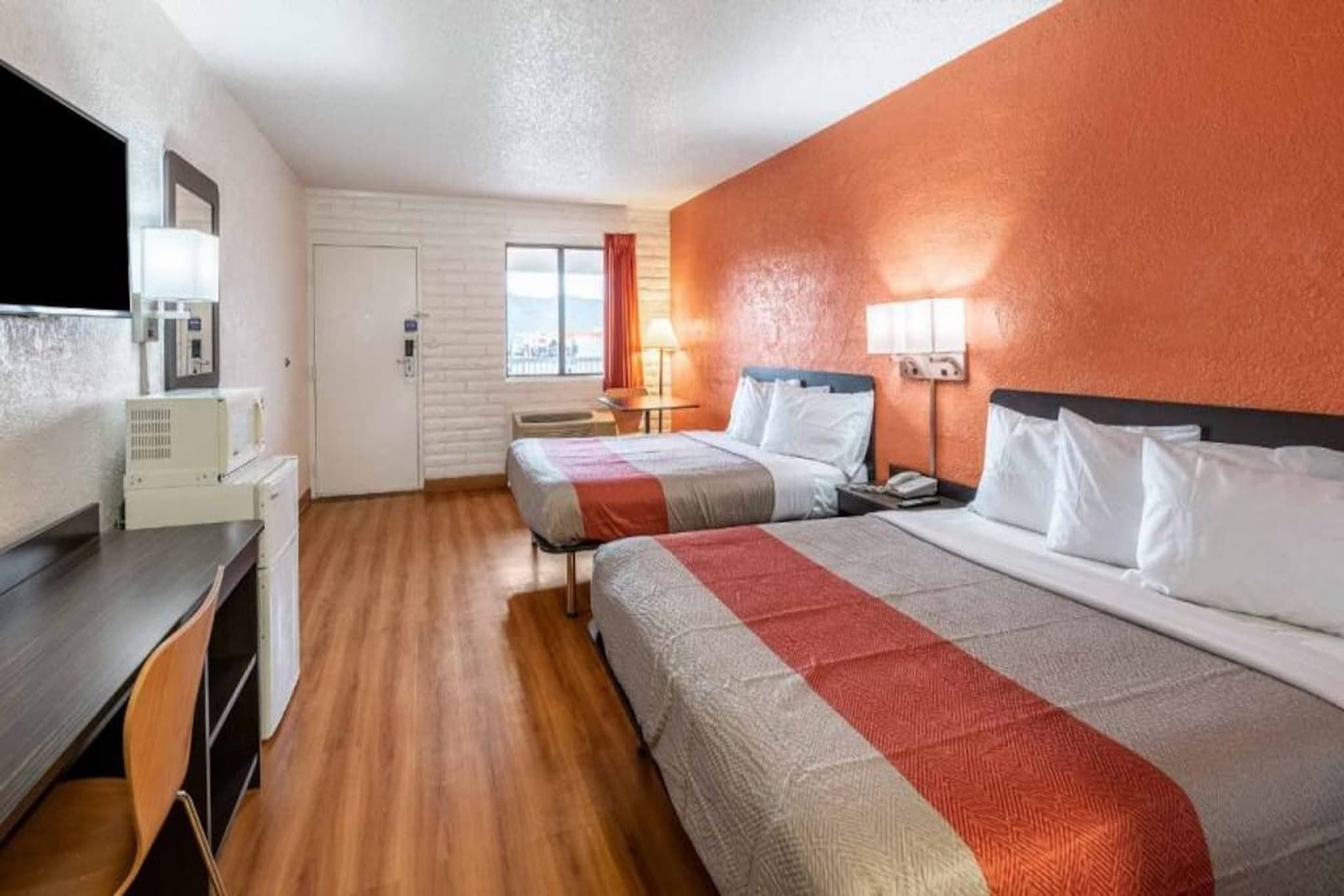 A hotel room with two beds, a desk, a television, and a window with curtains.