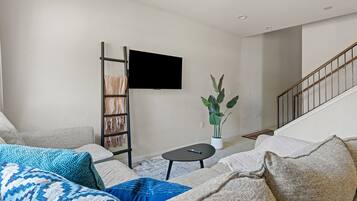 Una sala de estar con sofá, mesa de centro, televisor montado en la pared, una planta y una escalera.