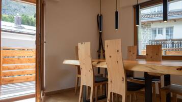 A dining area with a wooden table and chairs, a hanging light fixture, and a view of a mountain through a window.