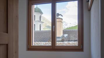 A room with a bench, a window with a view of a building and mountains, and a wooden door.
