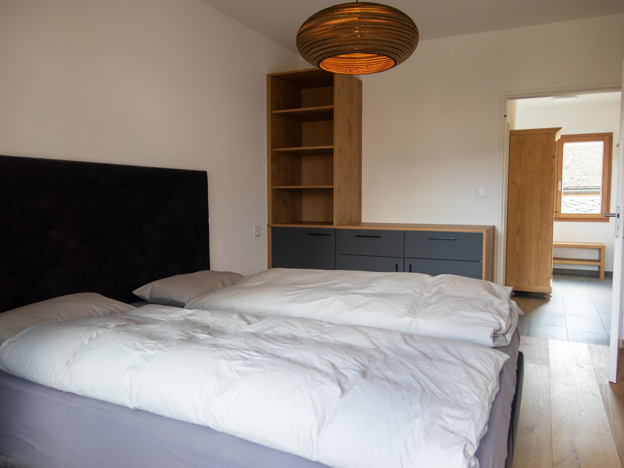 A bedroom with a bed, a wooden wardrobe, and a built-in shelf unit.