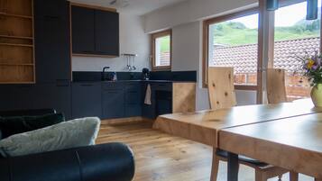A modern kitchen with dark cabinets, a wooden dining table, and a view of a green landscape through large windows.