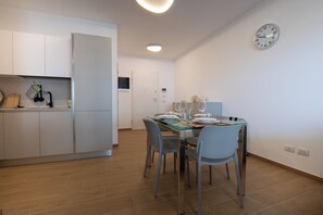 A modern kitchen with white cabinets, a dining table set for four, and a wall clock. - Modern and cozy apartment with views of the city and the Gran Sasso, featuring a spacious terrace (Pescara)