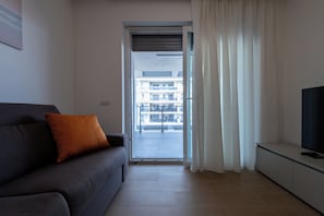 A modern living room with a grey sofa, a television on a stand, and a view through a sliding glass door to an outdoor balcony. - Modern and cozy apartment with views of the city and the Gran Sasso, featuring a spacious terrace (Pescara)