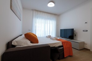 A hotel room with a bed, a TV, a desk, and a window with curtains. - Modern and cozy apartment with views of the city and the Gran Sasso, featuring a spacious terrace (Pescara)