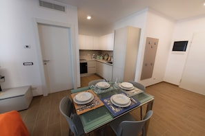 A dining area with a glass table set for four, surrounded by chairs. There is a kitchen in the background with cabinets and a microwave. - Modern and cozy apartment with views of the city and the Gran Sasso, featuring a spacious terrace (Pescara)
