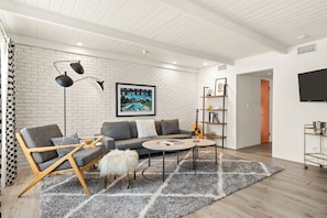 Un salon moderne comprenant un canapé, un fauteuil, une table basse et un téléviseur fixé au mur.