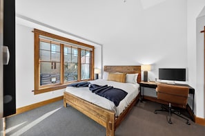 A hotel room with a large window, a bed with a wooden headboard, a desk with a computer, and a chair. - Mountain Views | Pool & Spa | Walk to Gondola | Village Dining | The Iron Horse (Truckee)