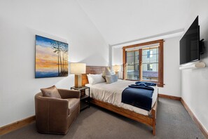 Ein Hotelzimmer mit Bett, Sessel, Gemälde, Lampe und Fernseher.