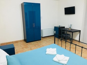 Een kamer met een bed, een bureau, een blauwe garderobe en een televisie aan de muur.