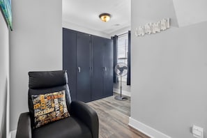 Quarto moderno com uma cadeira de couro preta, um ventilador portátil e um guarda-roupa com portas deslizantes.
