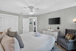 Quarto com cama, cadeira, televisão e ventilador de teto.