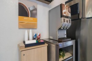 Una kitchenette con cafetera, taza de café y dispensador de azúcar.