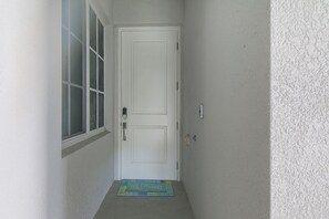 Ein schmaler Flur mit einer weißen Tür, einem Fenster und einer Fußmatte.