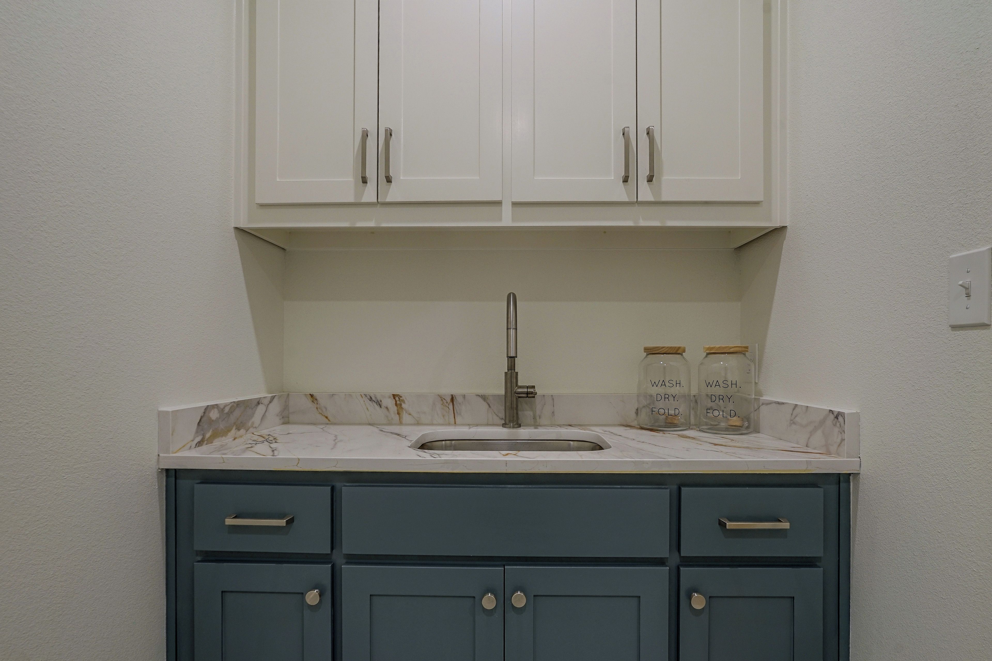 A kitchen with white cabinets, a sink, and two jars labeled 'WASH. DRY. FOLD.'
