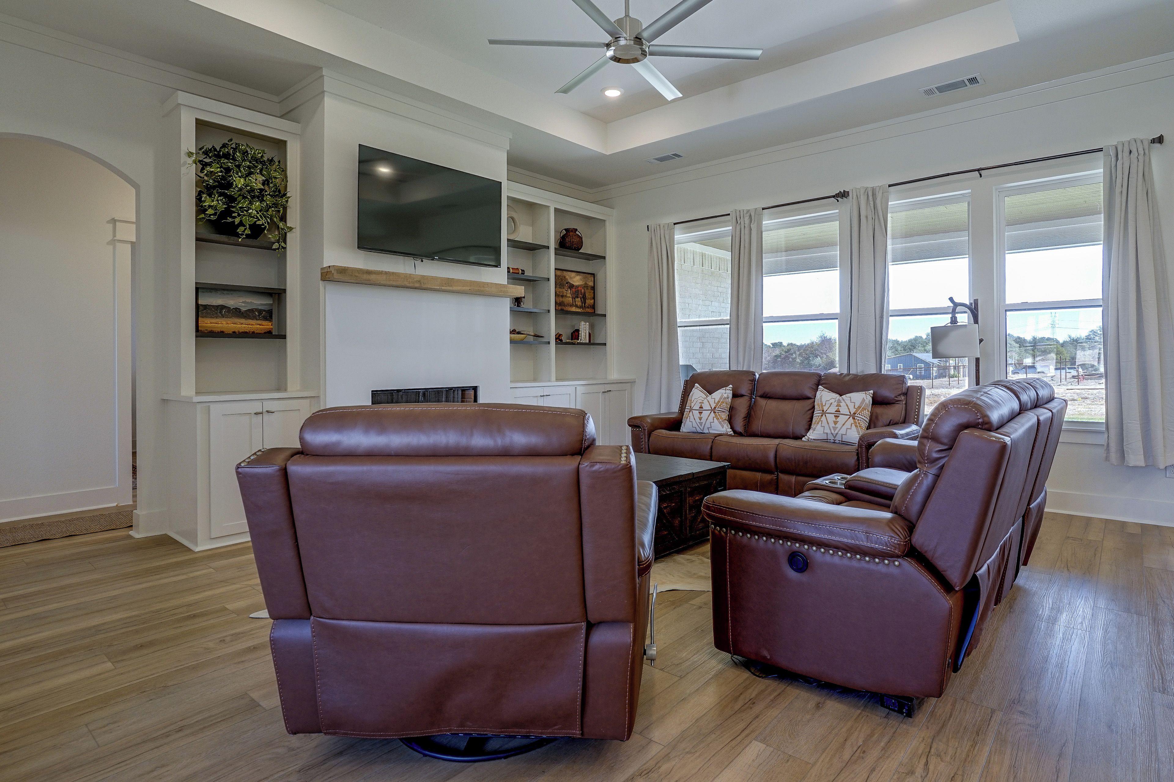 A modern living room with a sectional sofa, a flat-screen TV mounted on the wall, and a large window with curtains.