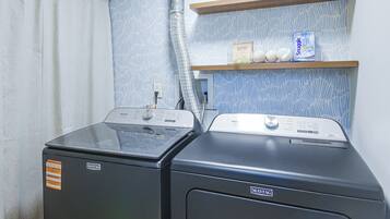 A laundry area with two Maytag washers and dryers, a shelf with laundry detergent, and a patterned wall.