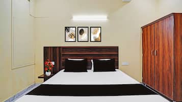 A hotel room with a bed, a wardrobe, a nightstand with a vase of flowers, and three framed pictures on the wall.