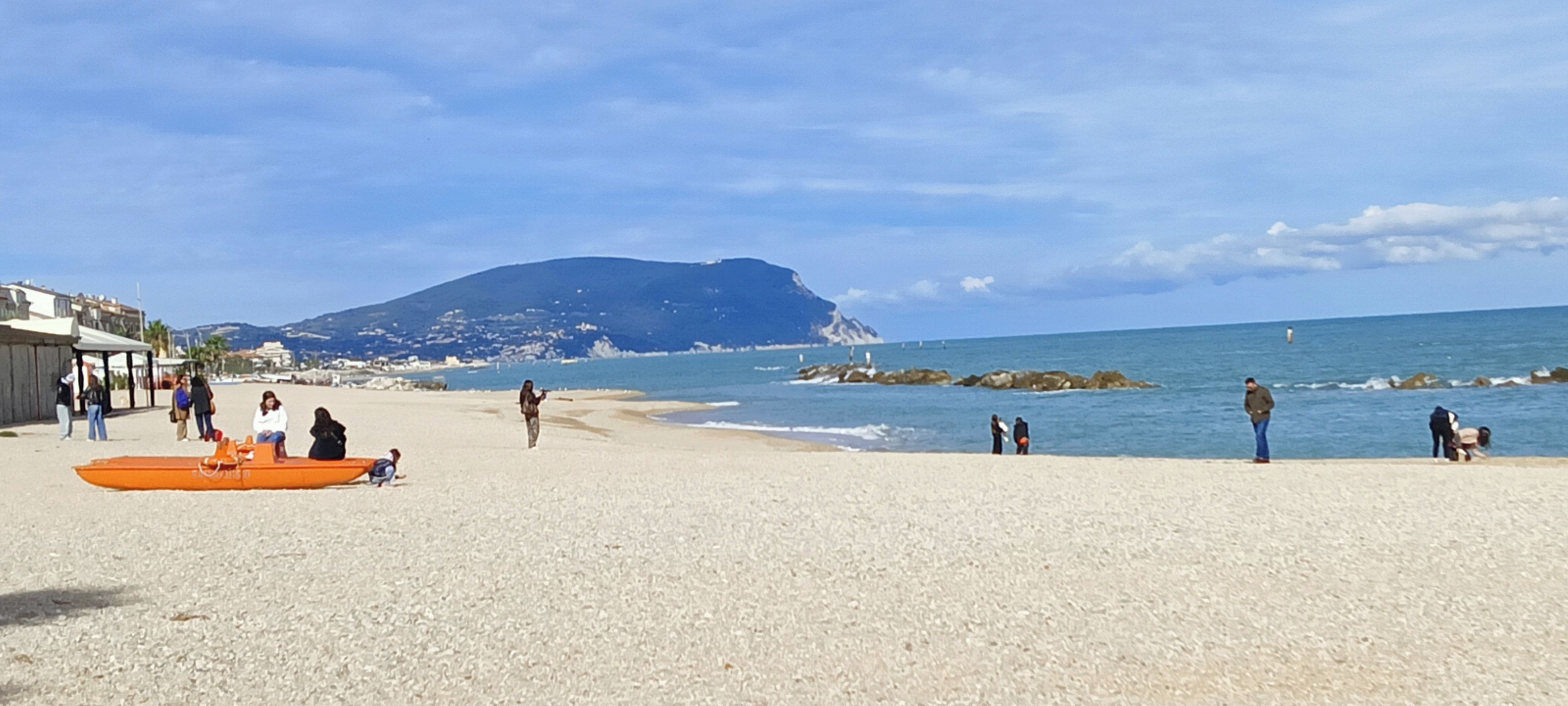 A beach with people, a mountain in the background, and a rocky shoreline.