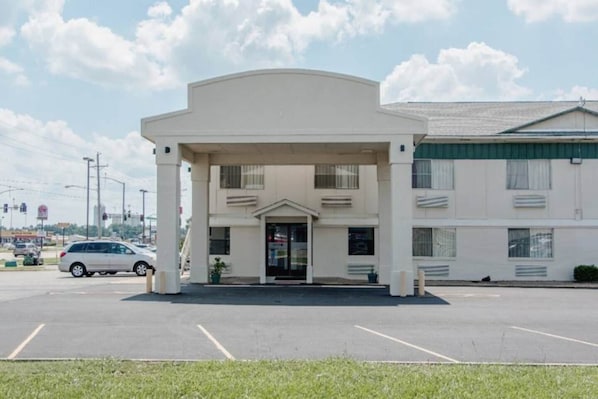 A building with a central entrance, a parking lot, and a vehicle in the foreground.