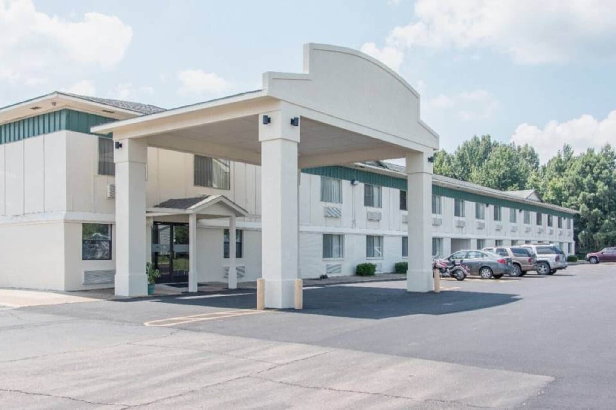 A motel with a covered entrance, multiple parking spaces, and a row of parked cars.