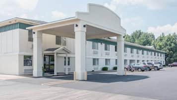 A motel with a covered entrance, multiple parking spaces, and a row of parked cars.
