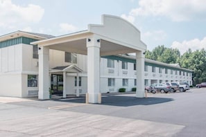A motel with a covered entrance, multiple parking spaces, and a row of parked cars.