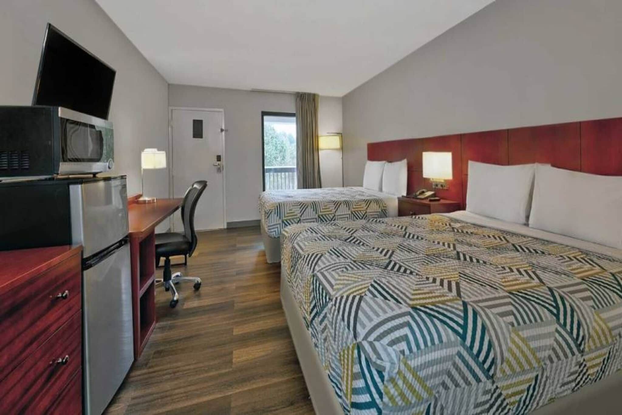 A hotel room with two beds, a desk, a chair, a television, and a refrigerator.