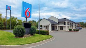 A motel with a large sign displaying the number 6, a parking lot, and a building with a flat roof and a single-story structure.