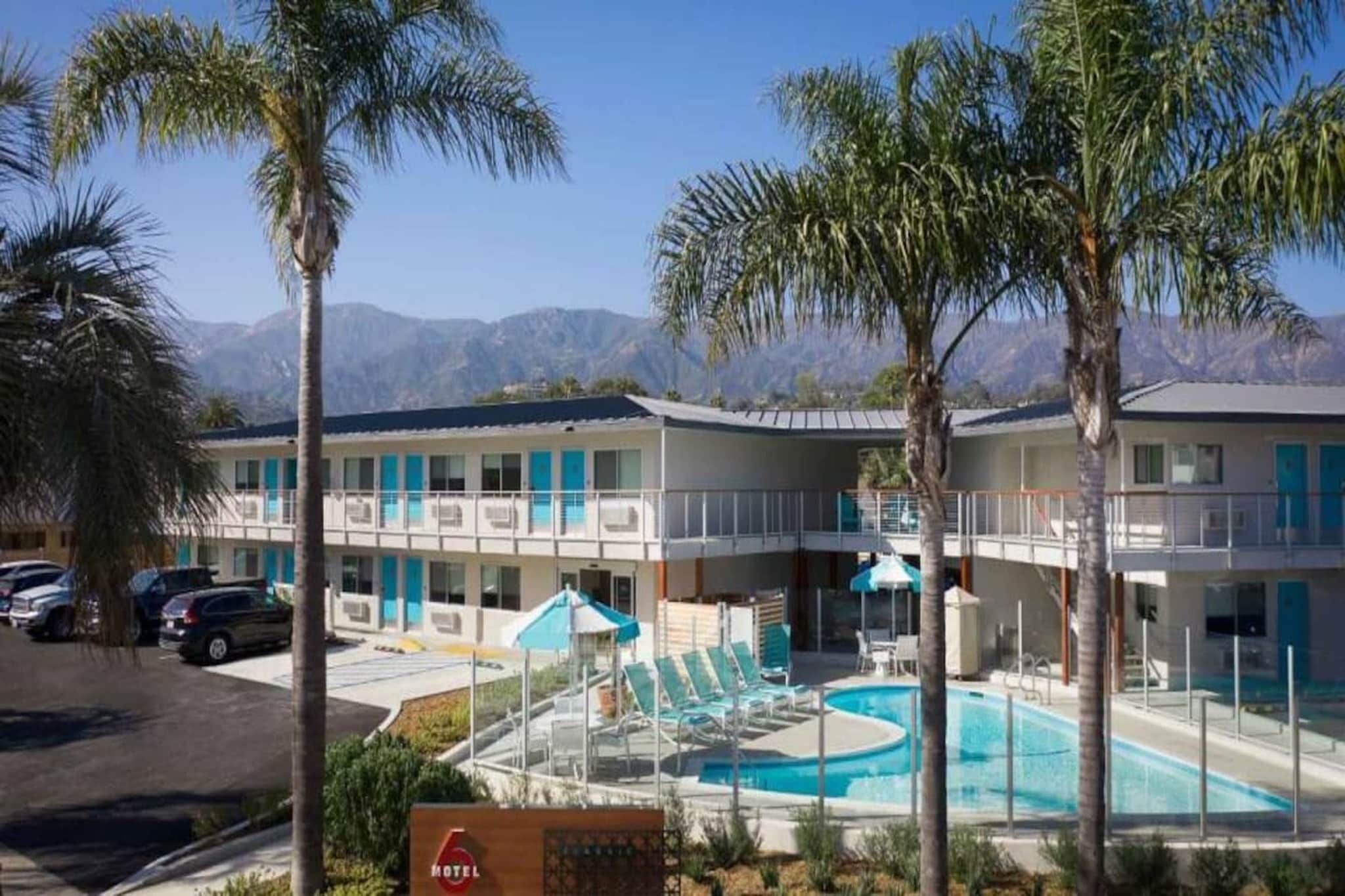 A hotel with a pool, palm trees, and mountains in the background.