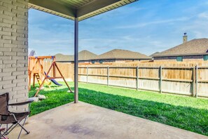 Een overdekte patio met een betonnen vloer, een houten omheining en een gazon.