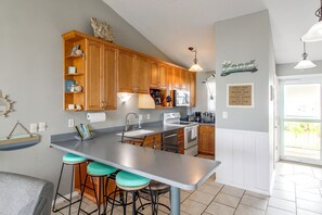 A kitchen with wooden cabinets, a stainless steel island, bar stools, a microwave, and a coffee maker. - Unwind Poolside, Walk to Beach! Pensacola Getaway (Pensacola)