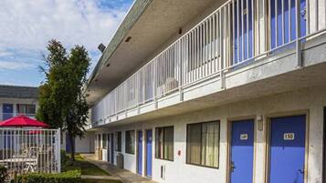 A multi-story motel with individual rooms numbered 149 and 150, a covered outdoor seating area, and a small garden.