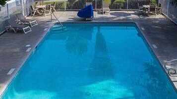 A rectangular swimming pool with a 5 ft depth marker, surrounded by a white fence, and equipped with lounge chairs and umbrellas.