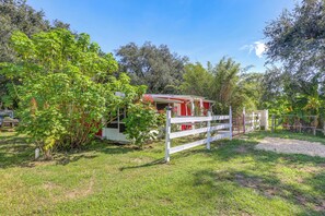A rustic cabin with a red exterior, surrounded by lush greenery and a white fence. - 6 Mi to Spanish Springs! Private Unit w/ Projector (Lady Lake)