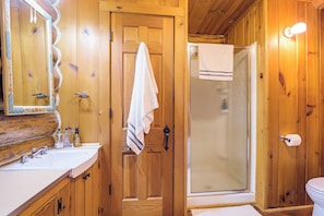 Ein Badezimmer aus Holz mit Waschbecken, Spiegel und Duschbereich.