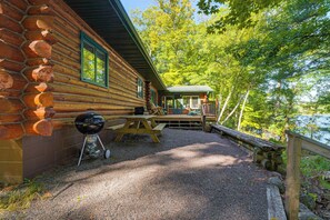 Eine Blockhütte mit einer Schotterauffahrt, die zu einer Holzterrasse führt.