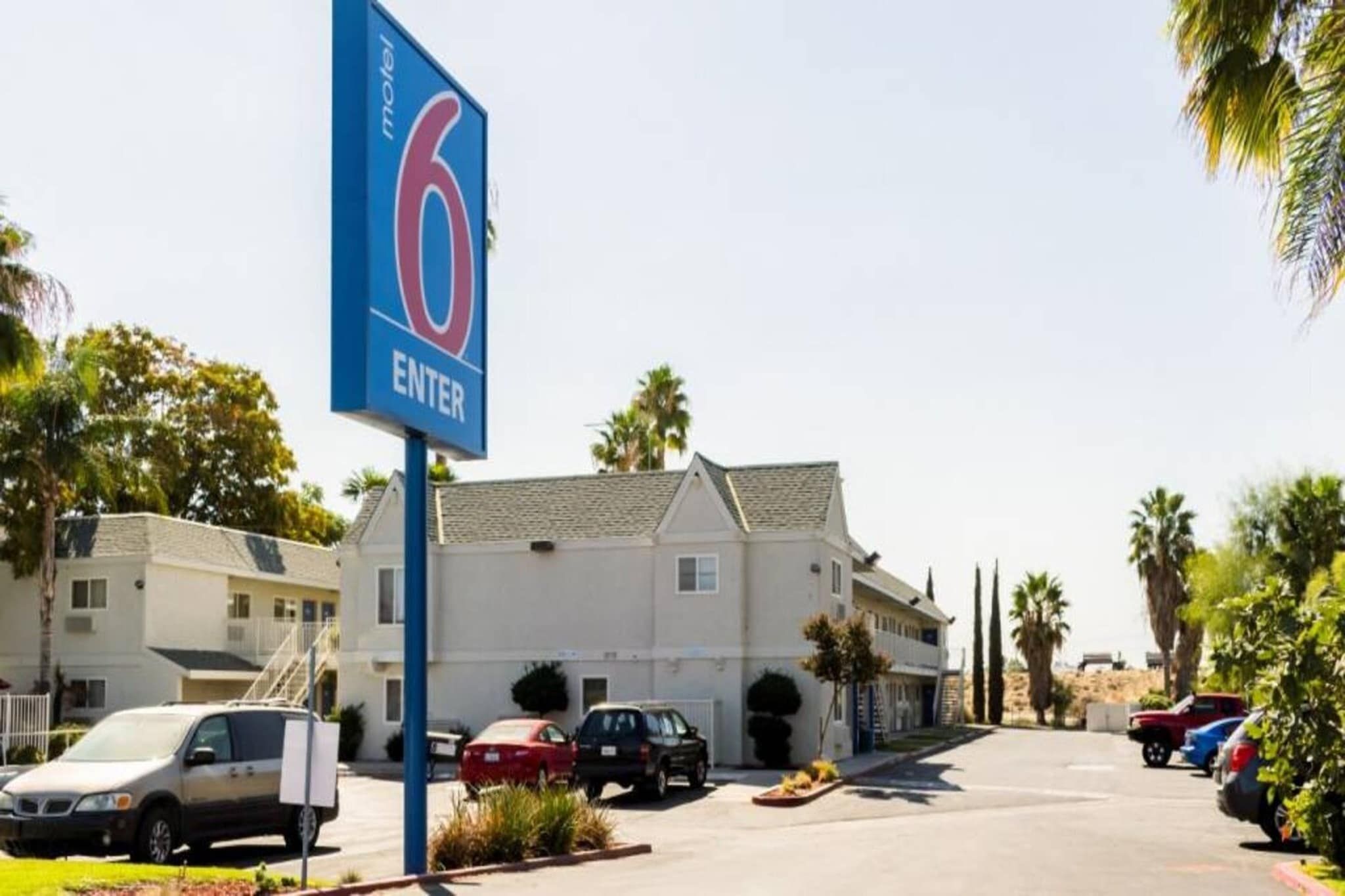 Um motel com um letreiro '6 ENTER', um estacionamento com vários carros e um prédio com telhado inclinado.