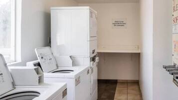 Uma lavanderia com máquinas de lavar e secar empilhadas, uma placa na parede e piso revestido de azulejos.
