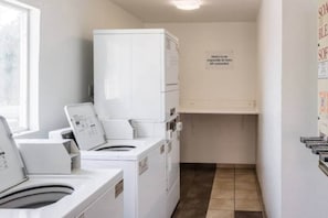 A laundry room with stacked washers and dryers, a sign on the wall, and a tiled floor.