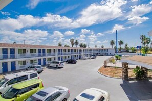 A motel with multiple rooms, a parking lot, and a clear sky. - Spacious ADA King Bed|Free Wifi (San Bernardino)