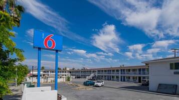 Un motel avec une enseigne bleue bien visible, sur laquelle figure le chiffre 6, un parking avec plusieurs voitures et une rangée de bâtiments du motel en arrière-plan.