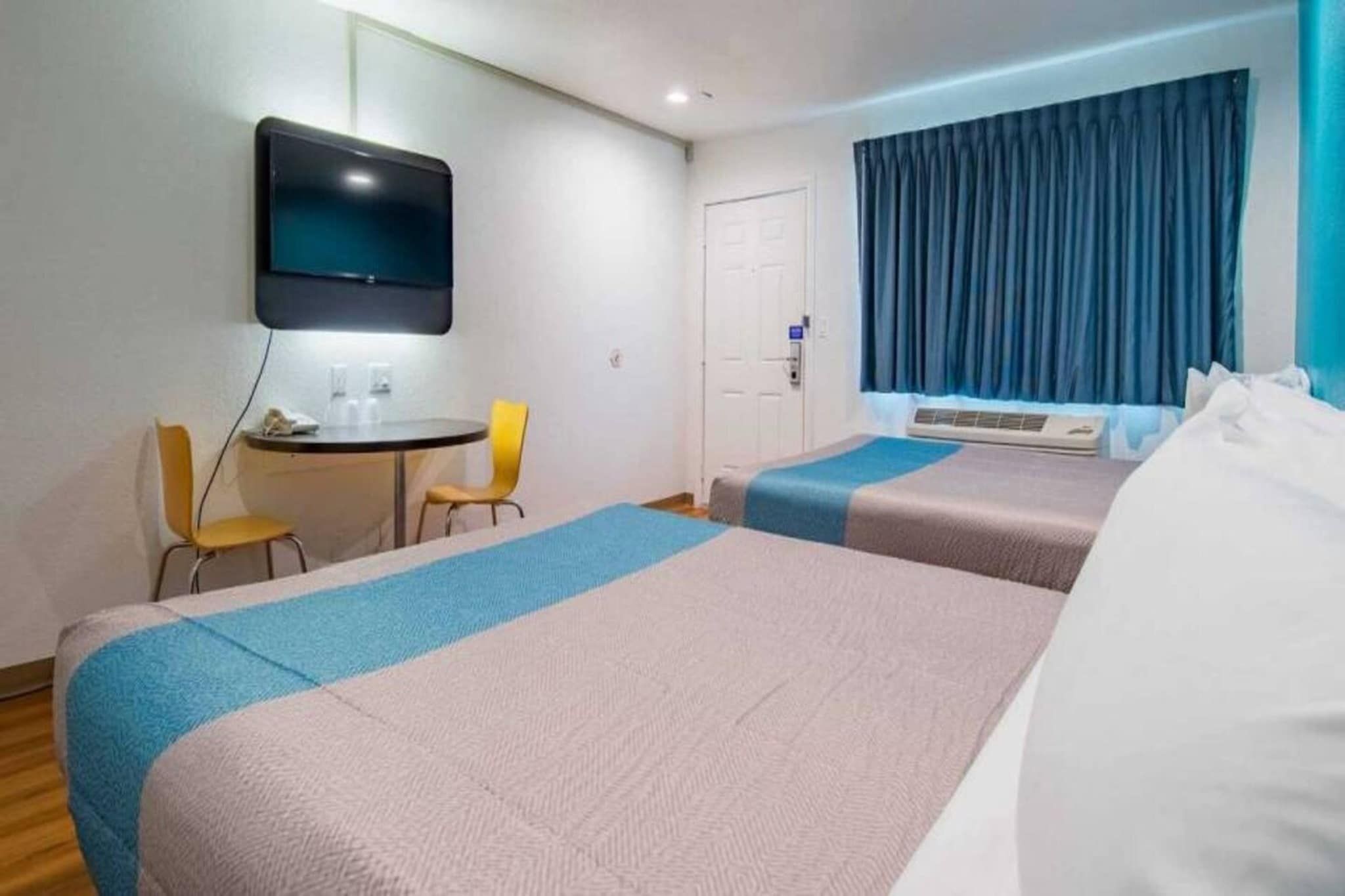 Et hotelværelse med to senge, et skrivebord, stole, et fjernsyn og et vindue med gardiner.