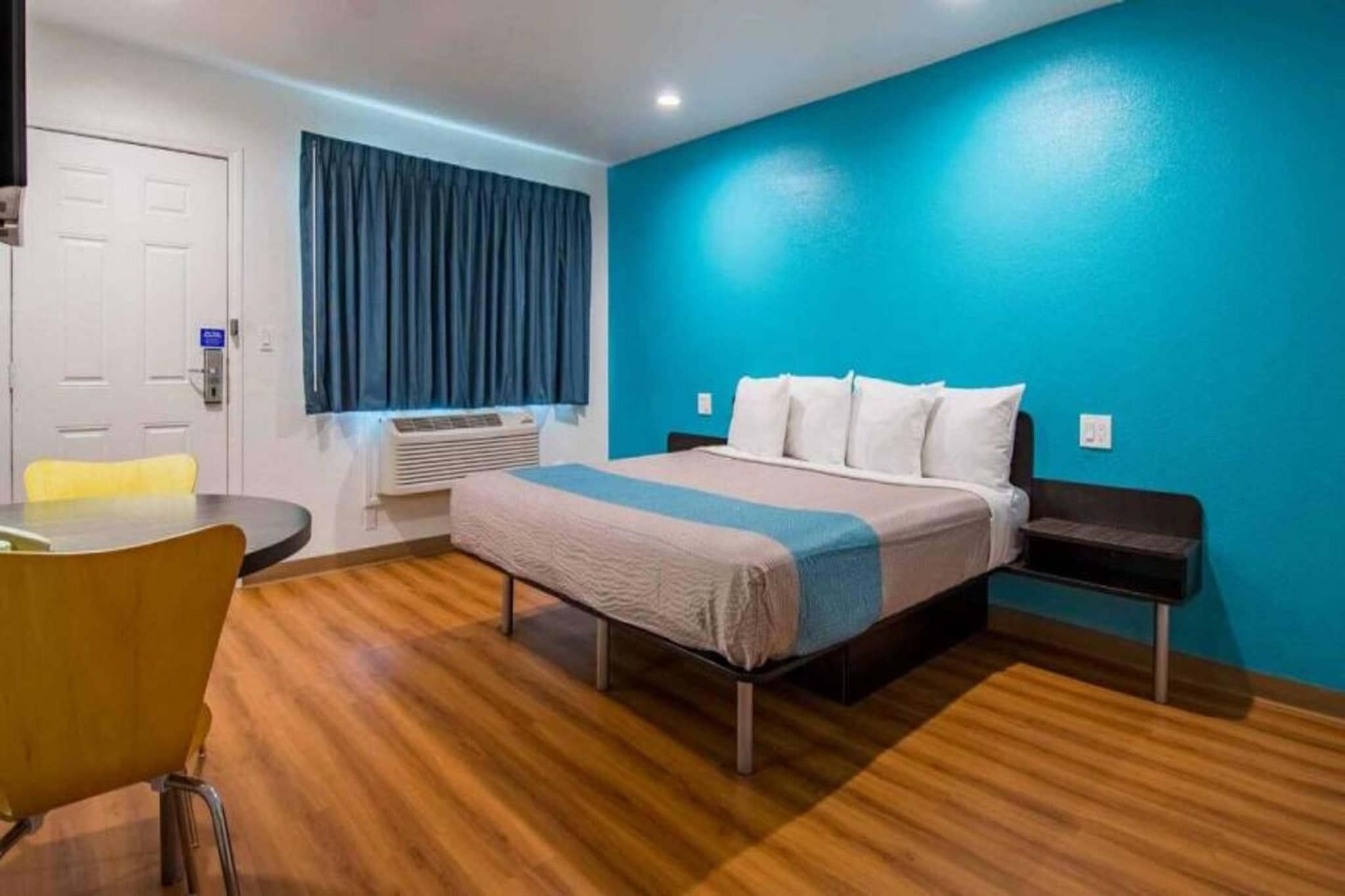 Una habitación de hotel con cama, mesita de noche, silla y equipo de aire acondicionado.