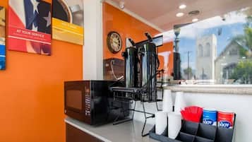 A coffee station with a coffee machine, cups, and a clock on the wall.